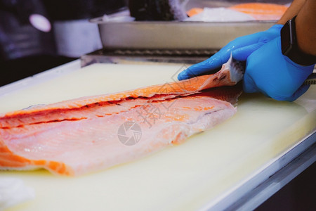 生的寿司切沙门鱼片主厨切开新鲜生鲑鱼片餐桌上的剪板有一把尖利刀手紧橙图片
