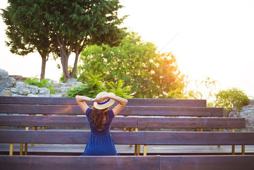 戴帽子的漂亮女孩坐在长椅上遇到戴着帽子的黎明美丽女孩坐在长椅上迎来黎明旅行天空人们图片