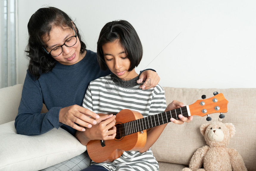 亚裔母亲教她女儿在自己家客厅沙发上坐时教她女儿玩乐游戏快可爱的童年图片