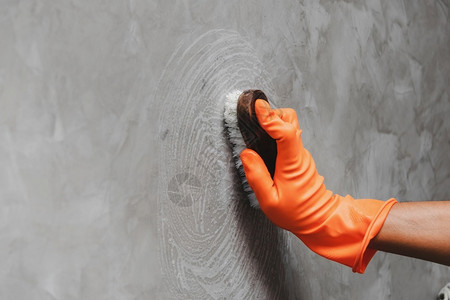 保护的戴橙色橡皮手套的人用来转换混凝土墙上的洗涤剂手臂屋图片