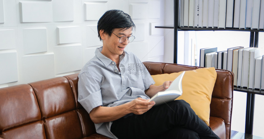 关心亚裔老人在家中客厅里读沙发的书亚洲老年男子的肖像正在放松和家阅读杂志时幸福快乐玻璃房间图片