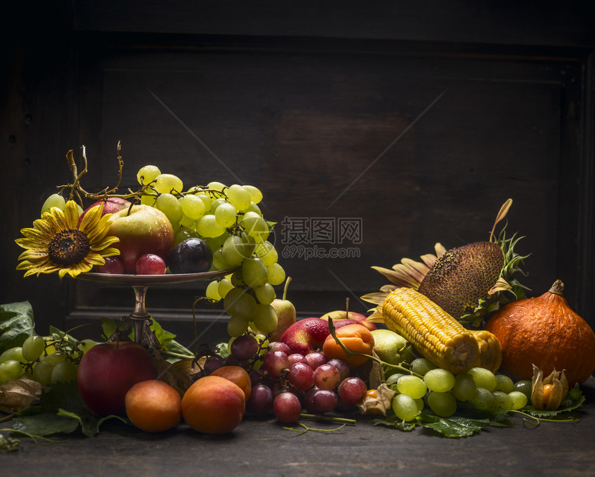 在一个铁碗中的葡萄苹果和秋季水及蔬菜在黑墙背景的木桌上放向日葵黄色的桌子自然图片
