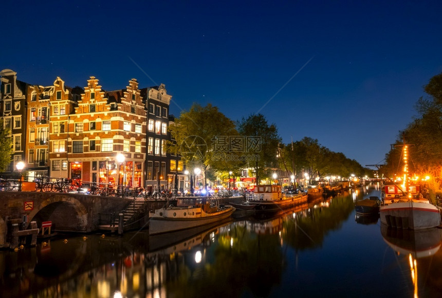 传统的城市景观荷兰在阿姆斯特丹住宅驳船和只的夜间运河上保持平静这些驳船停泊在传统房屋和阿姆斯特丹运河与夜间船舶和传统房屋之间的桥图片
