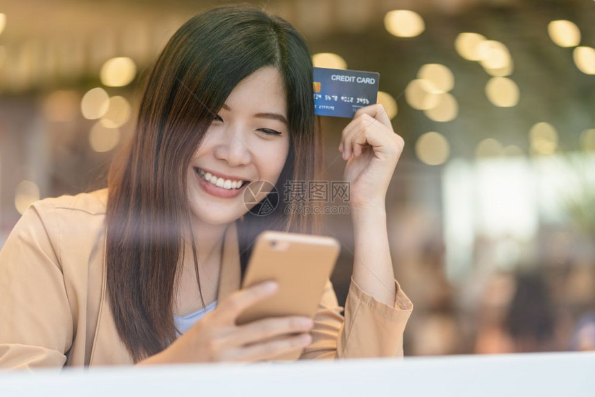 小样零售亚洲妇女利用信卡和移动电话在百货商店通过服装背景技术钱财包和网上支付概念信用卡模型在线购物亚洲妇女使用信卡和移动电话在服图片