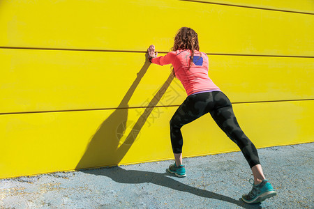 健康年轻的女子在跑之前爬黄色的墙壁上肌肉发达体操图片