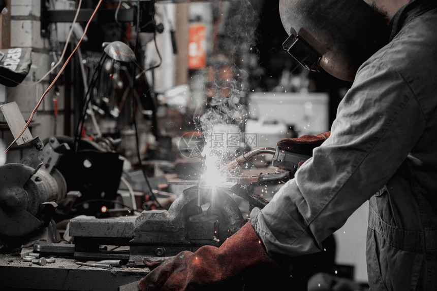 劳动者焊工正在用防护面罩焊接车库中的金属零件工业钢焊作机正在用防护面罩焊接车库中的金属零件工业钢焊机框架男图片