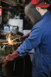 火花抽烟劳动者焊工正在用防护面罩焊接车库中的金属零件工业钢焊作机正在用防护面罩焊接车库中的金属零件工业钢焊机图片