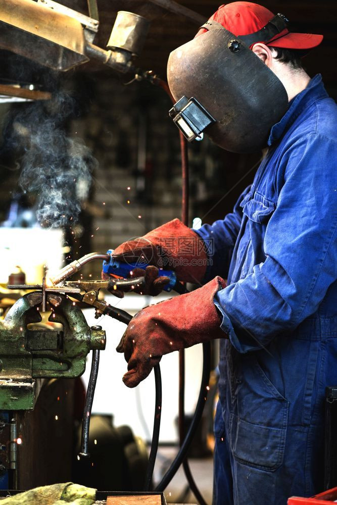 焊工正在用防护面罩焊接车库中的金属零件工业钢焊作机正在用防护面罩焊接车库中的金属零件工业钢焊机劳动者火花氩气图片