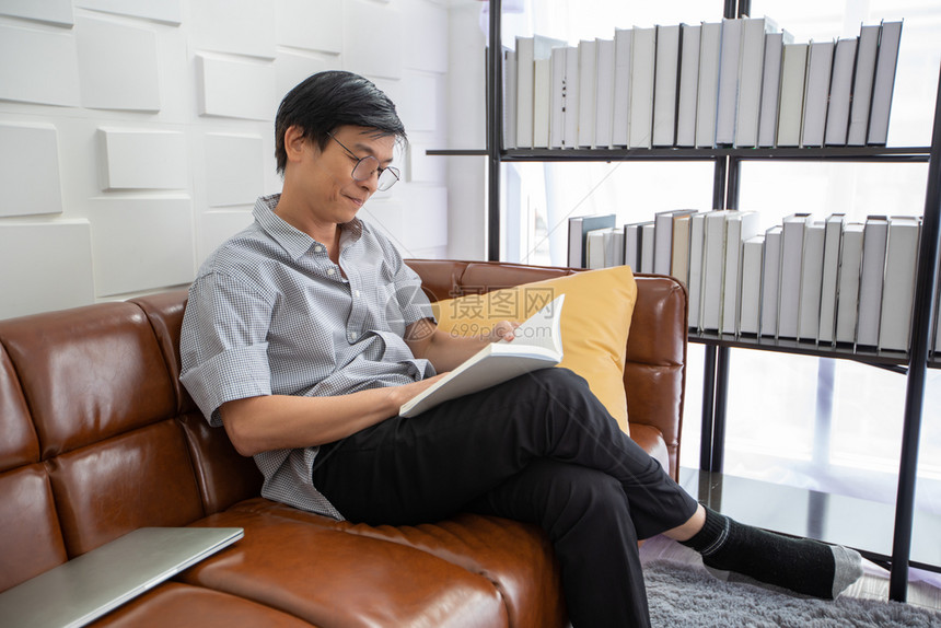 在室内娱乐亚裔老人在家中客厅的沙发上读书亚洲老年男子的肖像正在放松和幸福与阅读杂志男图片