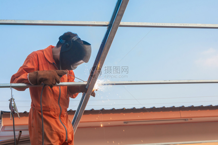 部件将工人焊接在橙色作服中焊接面具桁架图片