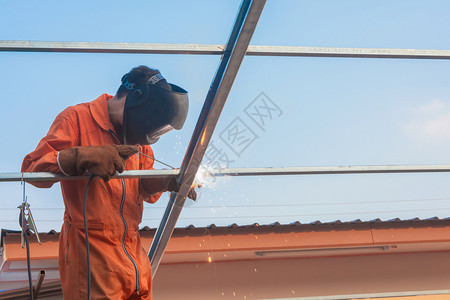 部件将工人焊接在橙色作服中焊接面具桁架图片