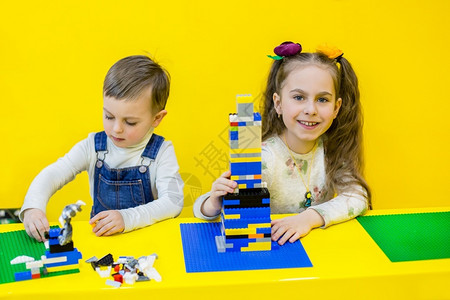 学习在黄色背景上玩构造器的四胞胎Siblings正在玩构建器愉快俏皮图片
