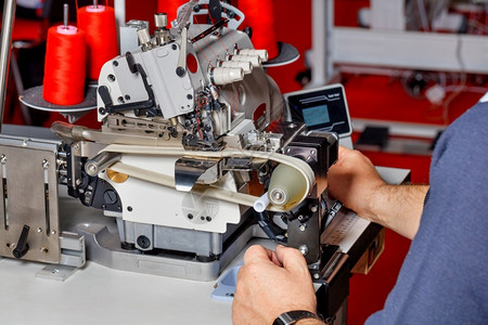 机器缝衣生产手和工匠建立现代电动缝纫机检查其工作质量师傅调整现代电动缝纫机的工程a管理者对现代电动缝纫机的工作进行调整现代的接缝背景图片