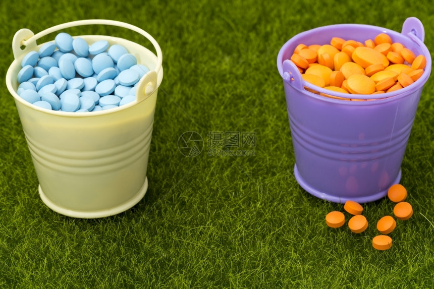 制药概念两个装满橙色和蓝药丸的桶两个装满橙色和蓝药丸的桶在绿草上丰富多彩的宽慰医疗图片