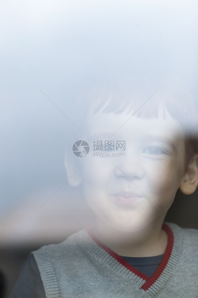 一种在后面可爱的小男孩在看着一栋大楼的玻璃杯后面照相机看着一个成年人去工作一个带着微笑的男孩肖像一个小男孩图片