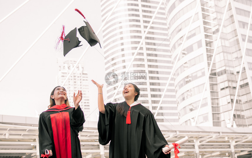 两名身穿制服的亚洲女学生在毕业后微笑着快乐和扔起帽子并带着笑容和欢的喜悦投掷庆典图片