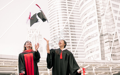 两名身穿制服的亚洲女学生在毕业后微笑着快乐和扔起帽子并带着笑容和欢的喜悦投掷庆典天空高清图片素材