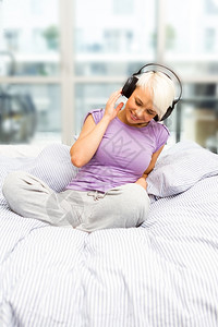 放松快乐金发微笑的女人正在听音乐床上耳机的随意图片