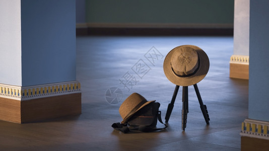 淑女帽阴凉处关注挂在摄像三脚架上的女士帽挂在黑色照相袋上的Fedora帽子用古老音调风格的木地板上以蓝柱为基底的色子双头饰旅行概念目的背景