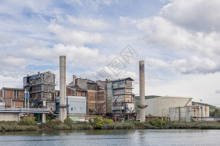 旧化工厂在河岸边有烟囱和井仓管道银行建筑物背景图片