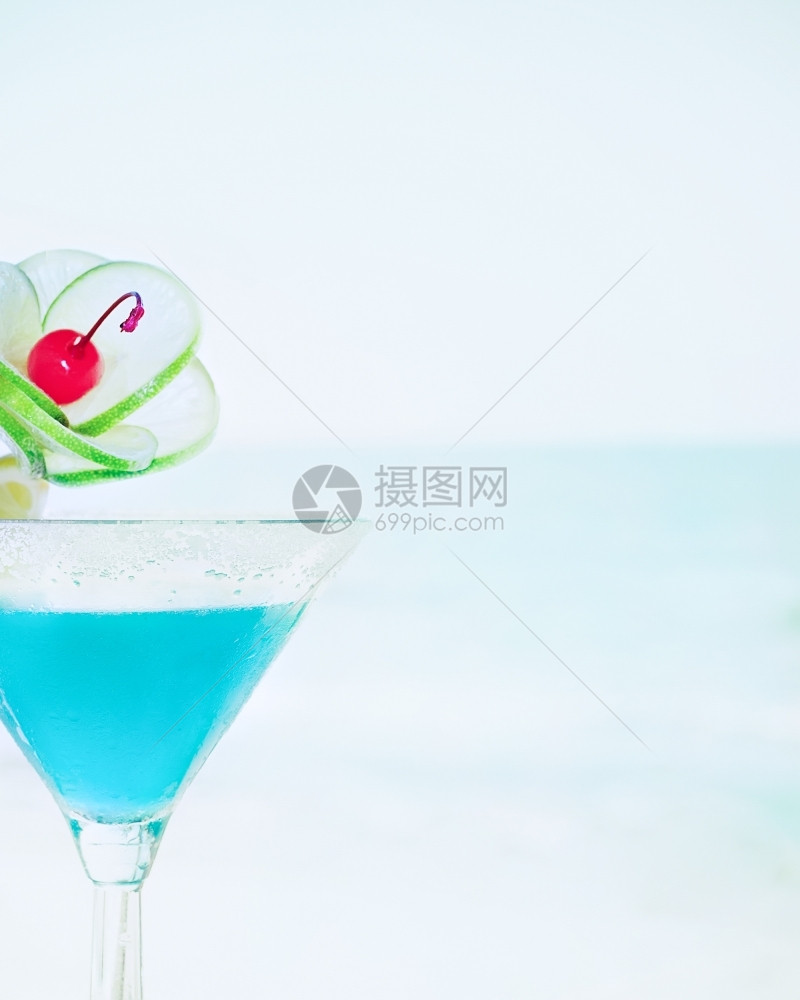 冰镇蓝色玛格丽塔鸡尾酒在热带海洋滩的滨上配有石灰水果和樱桃装饰品的蓝色玛格丽塔鸡尾酒派对食物图片