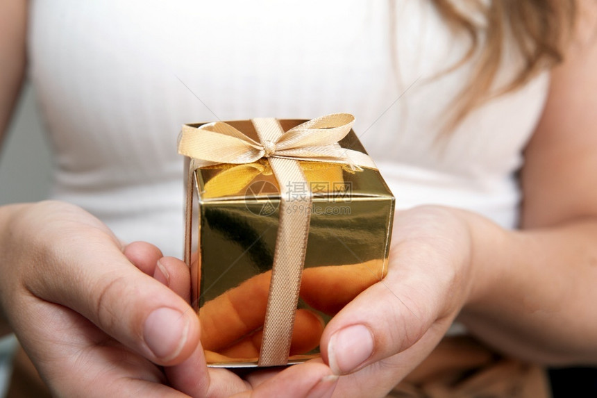 拿着金色礼盒的女人表示母亲节圣诞生日礼物概念柔和自然色彩背景休闲女人拿着金色礼品盒姿态给予母亲节生日礼物概念柔和自然色彩背景复制图片