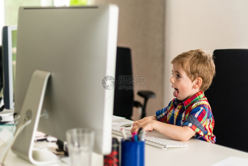 小工具男孩坐在办公椅上玩电脑展示他的舌头反映出集中现代装置和通信的概念简洁易用和可儿童坐在办公室椅子上显示他的舌头反映了专注坐着图片