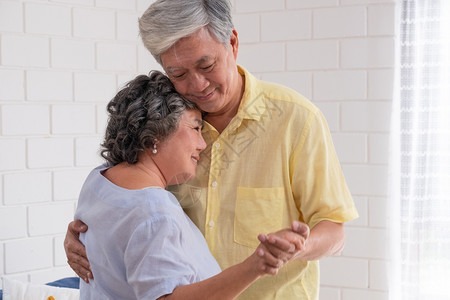快乐的亚洲老年情侣在客厅享受慢舞与温暖的爱和激情曾祖母亲吻父跳舞闲暇女背景图片
