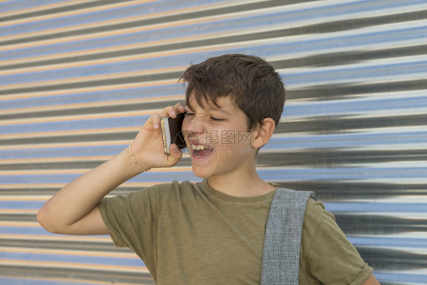 快乐男孩使用手机背着包回到学校概念中来玩的开心男孩书包城市聪明的图片