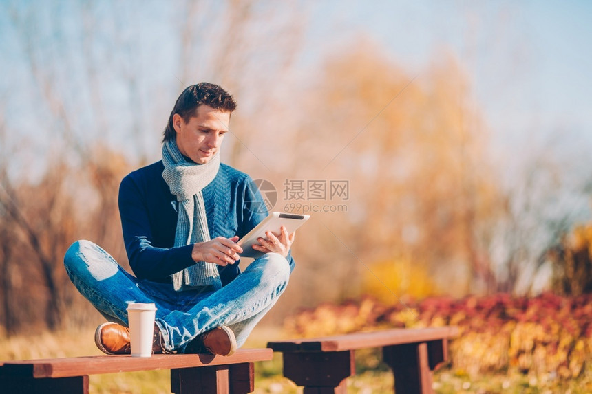 温暖的快乐笔记本电脑在秋天公园喝咖啡的快乐男人在秋天公园下的叶子青年男人在秋日公园户外用电话喝咖啡图片