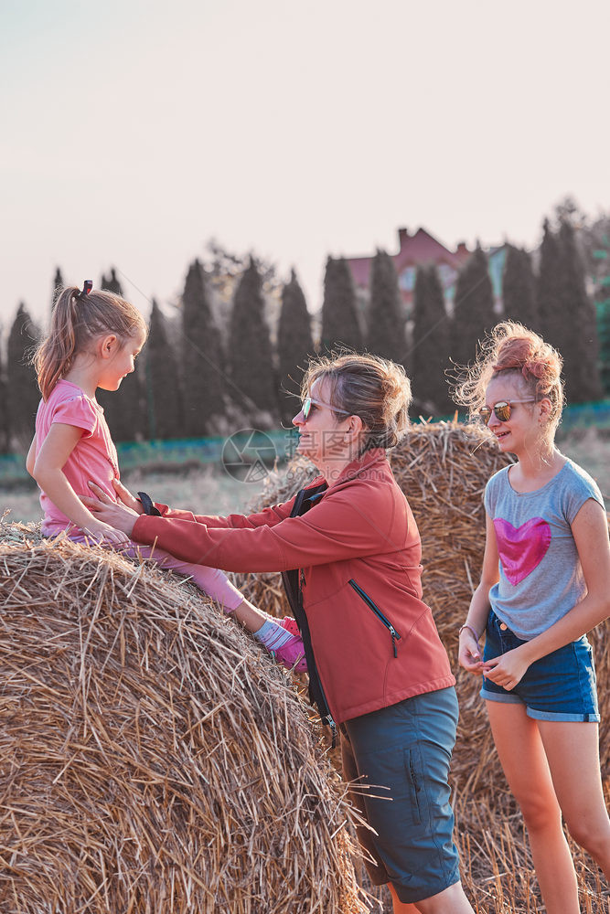 人们母亲和她的女儿十几岁孩和她妹一起在户外的干草堆上玩耍在乡村度过假期坦率的人真实时刻情况孩子们图片