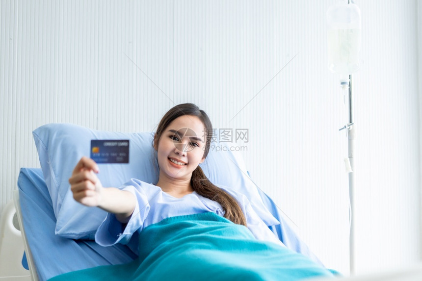 亚洲年轻女患者在展台上微笑的脸持有一张信用卡躺在房间医院背景的床上支付医疗费概念治用银行业护士医生图片