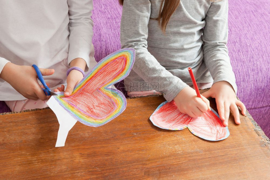 小女孩正在为母亲日或父情人节生画红和多彩的心胸红父亲们纸图片