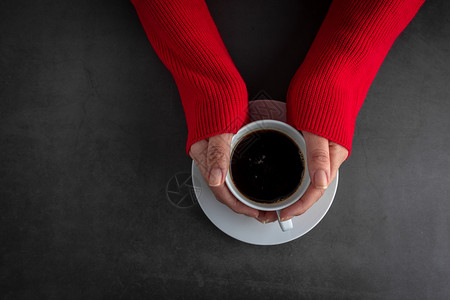 咖啡店泡沫身穿红色跳伞的女她双手在石头背景上举着一杯咖啡的热黑色图片