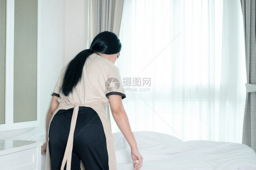 干净的站立年轻亚洲女佣在旅馆房间的床上铺毯子室图片