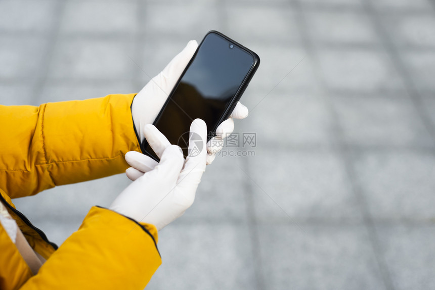 Corona传播预防措施概念在公共场所的街上持有移动电话的年轻妇女手持移动电话身着乳胶保护手套在街头佩戴乳胶保护手套在公共场所的图片