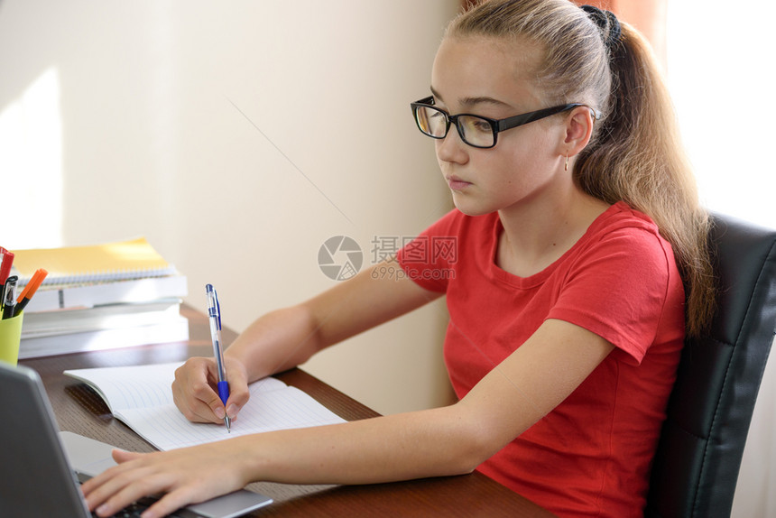 在笔记本电脑上做功课的戴眼镜女学生图片