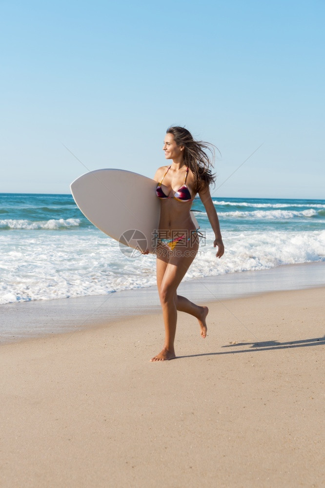 海滩上冲浪女孩拿着她的冲浪板奔跑图片