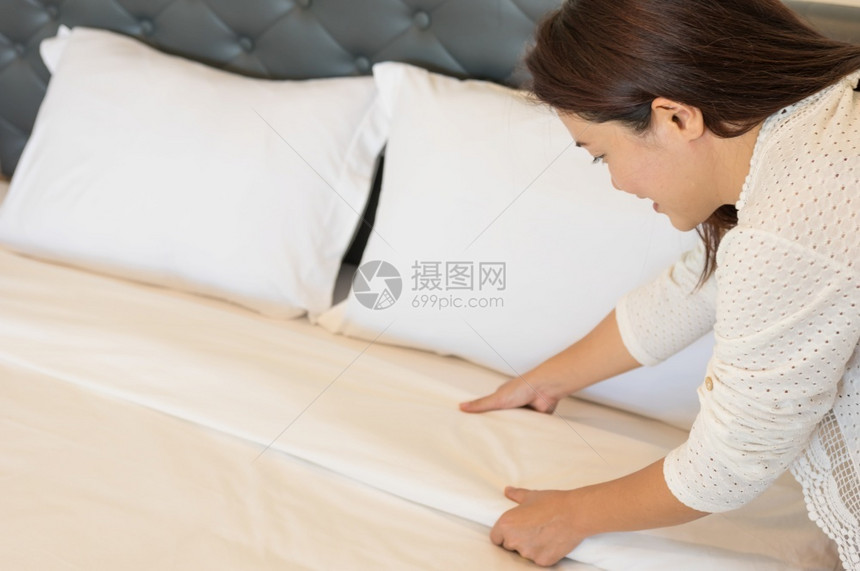 白种人家假期年轻的旅馆女青在干净的房间里准备床上有干净白毯子卧室有枕头和床单早上睡衣用软毛巾图片