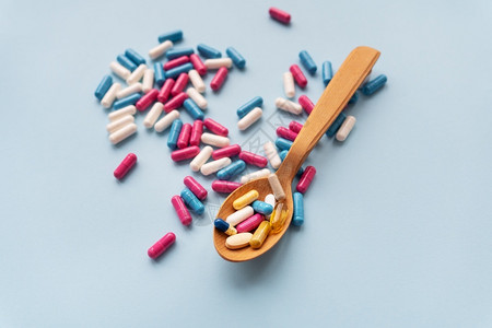 药品蓝色背景上的各种药丸和木勺其中维生素帮助医疗的图片