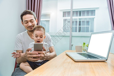 亚洲父子在家中一起使用智能手机和电脑图片