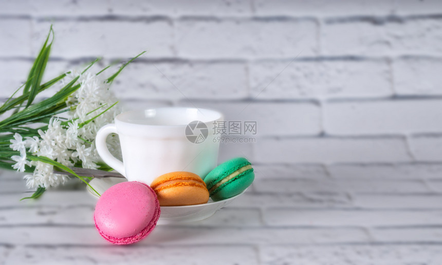 春天热的马卡龙杯上加茶餐桌的蛋糕和背景白花有彩色木桌配茶和花图片