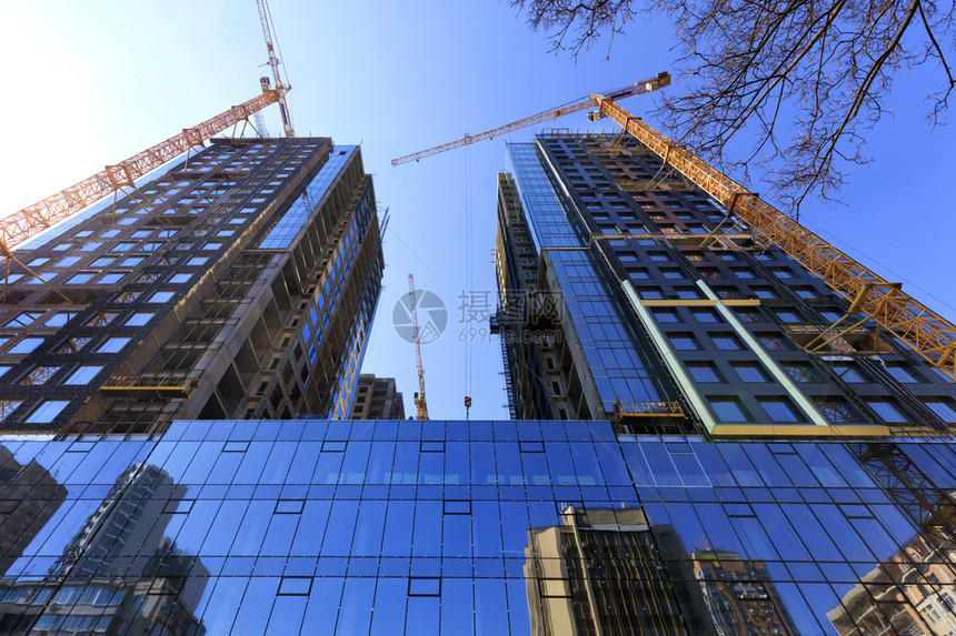 真实的以玻璃和混凝土制成的现代建筑表面碎片反映在相邻建筑物的玻璃墙壁上高塔建造吊机向上倾斜玻璃面是蓝色天空的反射物在正修建的现代图片