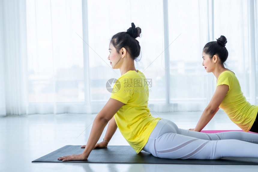 姿势两名亚洲年轻妇女在健身房练习瑜伽穿黄色礼服或与训练员和实习者一起表演冥想健康生活方式和健康概念手老师图片