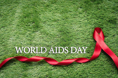 团结一致抗艾滋在绿草上的标志AIDS意识信号红丝带庆祝疾病背景