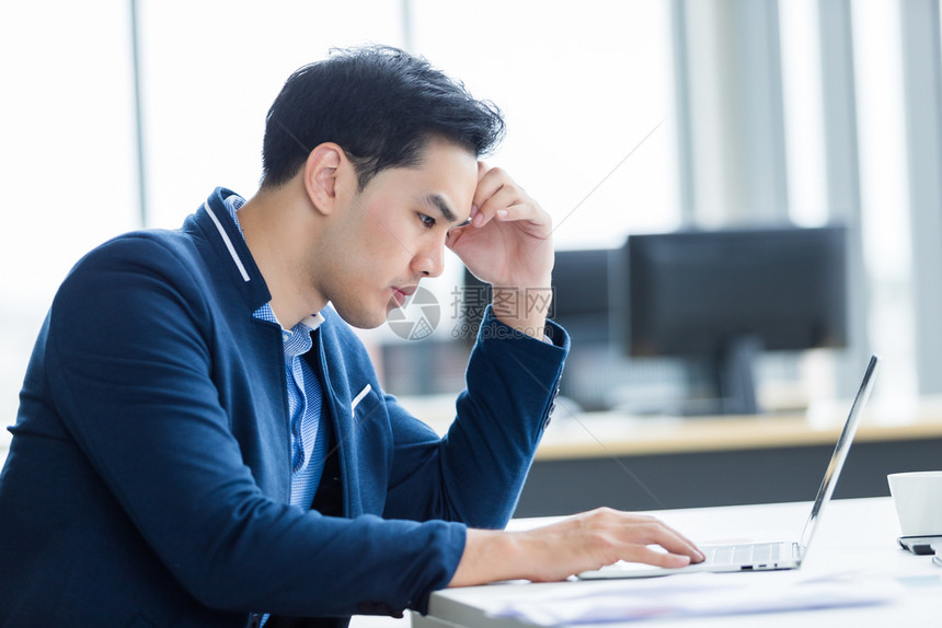 坏的白种人累精神紧张的商人从事笔记本电脑工作在商业损失后头痛在办公室背景中图片