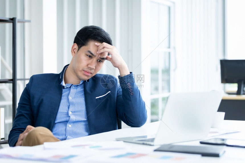 精神紧张的商人从事笔记本电脑工作在商业损失后头痛在办公室背景中英俊的行政人员沮丧图片