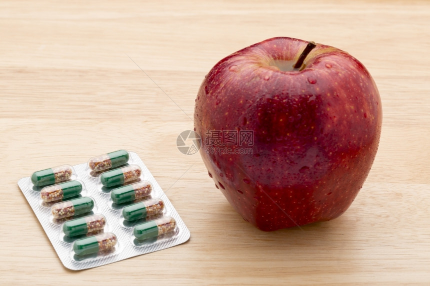木质背景上的绿色胶囊包装和新鲜红苹果绿色胶囊包装和新鲜红苹果抗生素关心未剥皮图片