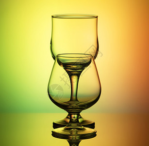 薄的葡萄酒和白格纳克兰地的杯子后面有一个细长的轮廓形拱门后面是黄绿色背景的亮空眼镜背绿景的空眼镜明亮目背景图片