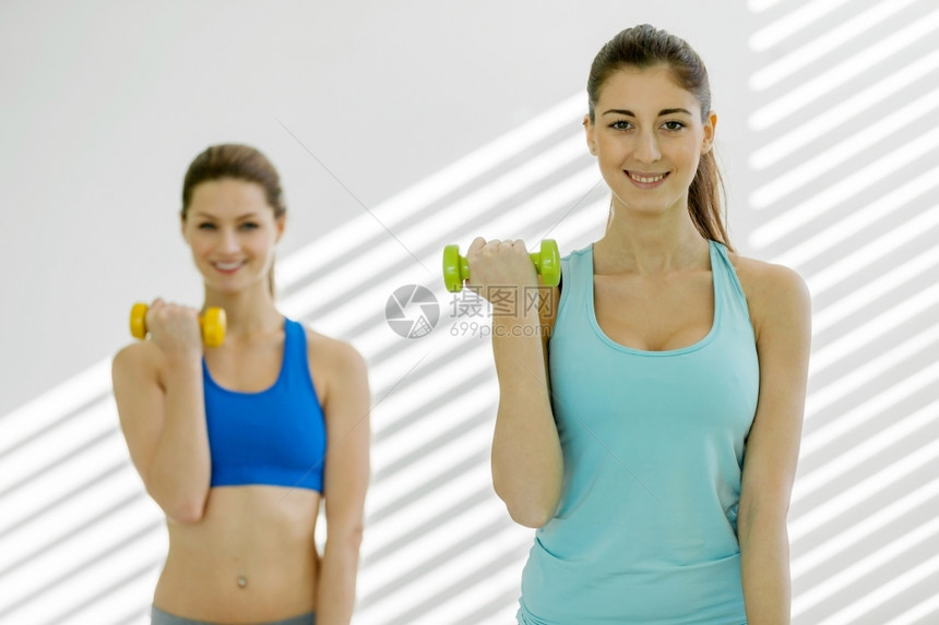 活力吸引人的运动型两名有吸引力的年轻女子在健身房做哑铃运动的照片图片